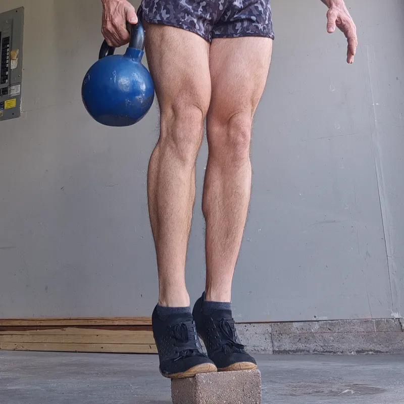 Standing calf raise with the toes on a garden stone and a kettlebell in one hand