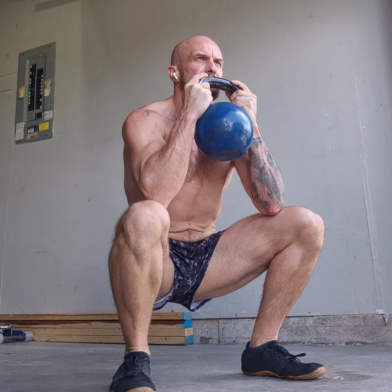 Deep goblet squat holding a kettlebell at chest height in a garage